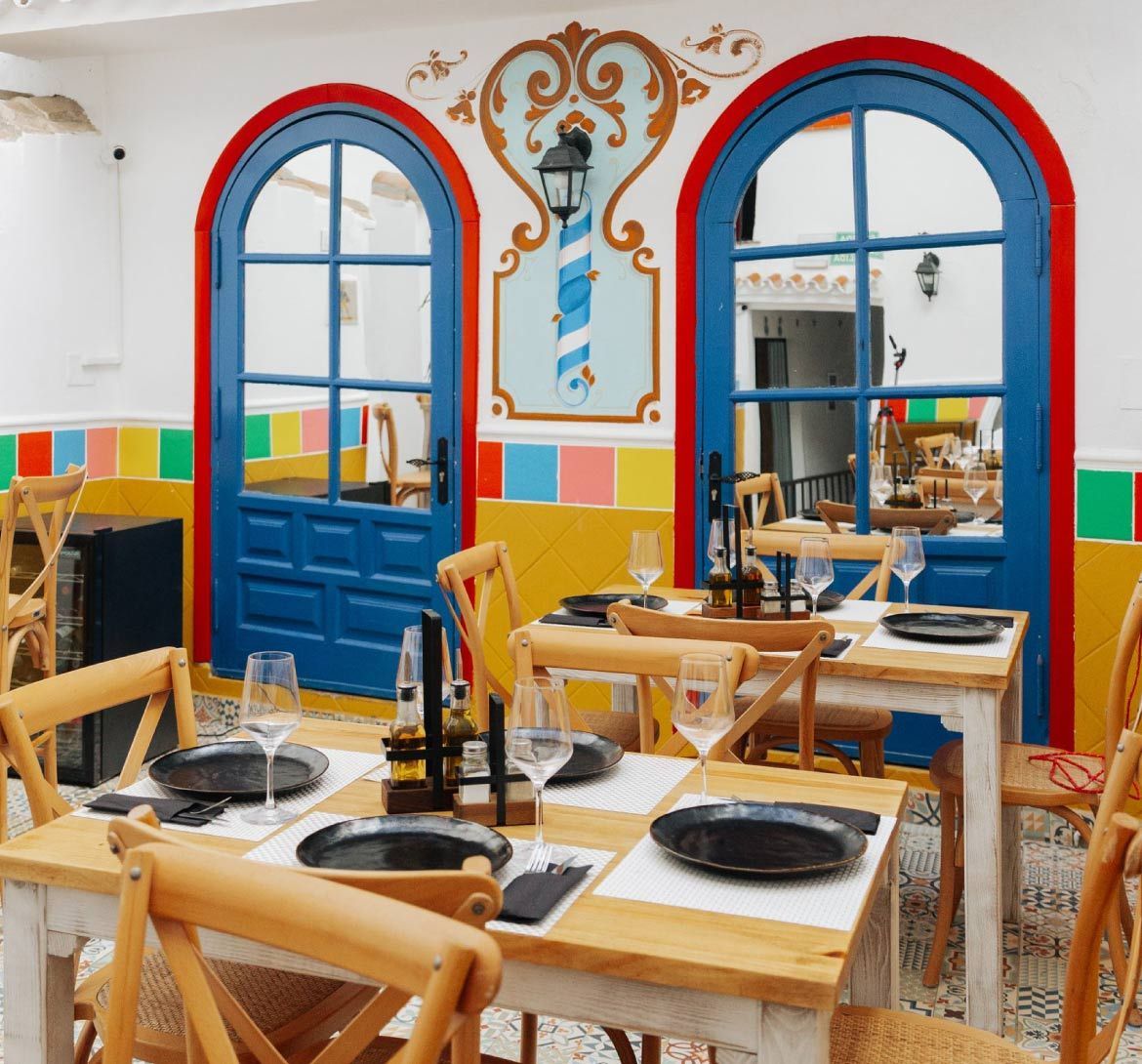 Interior de restaurante colorido con puertas azules y mesas de madera dispuestas para cenar.
