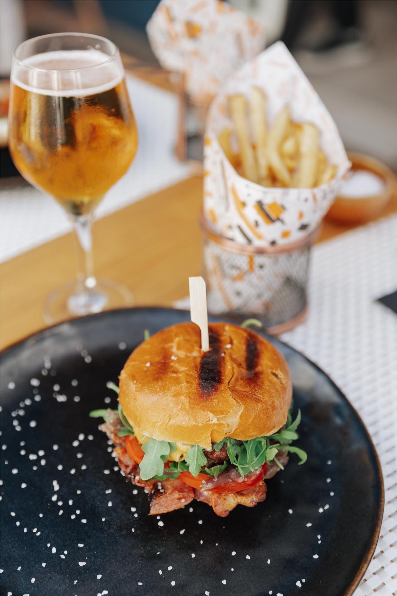 Hamburguesa con patatas fritas y cerveza en una mesa en un restaurante al aire libre.