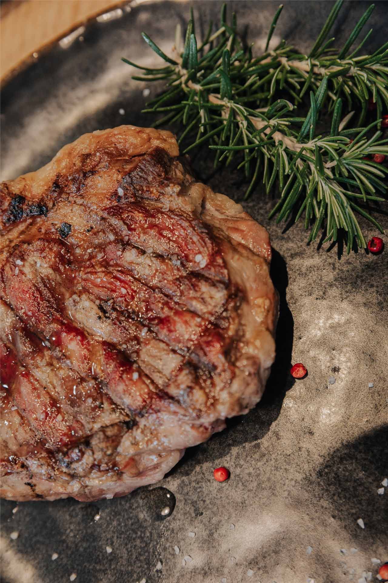 Filete a la parrilla en un plato oscuro, adornado con romero y granos de pimienta rosa.