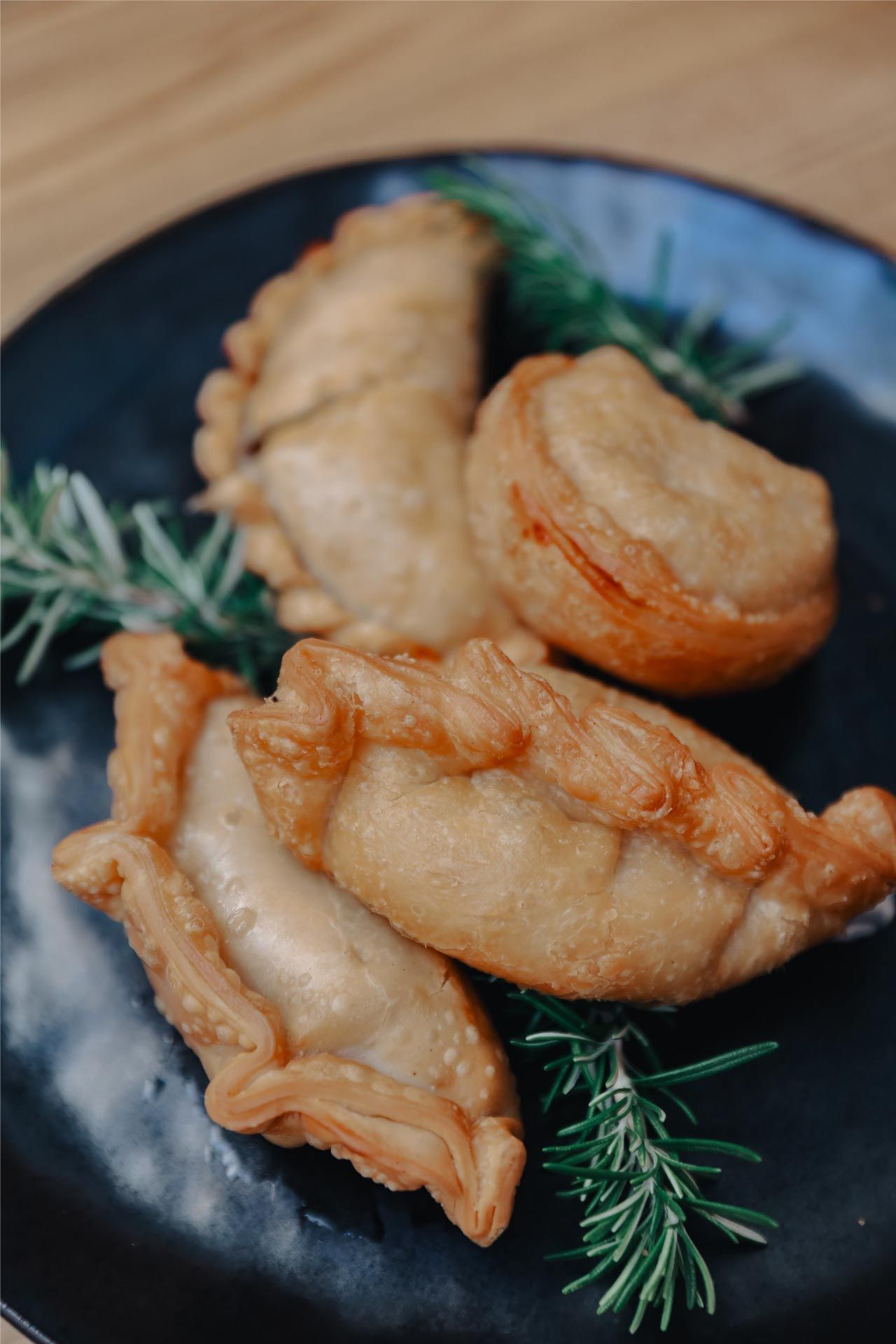 Empanadas fritas en plato negro con ramitas de romero.