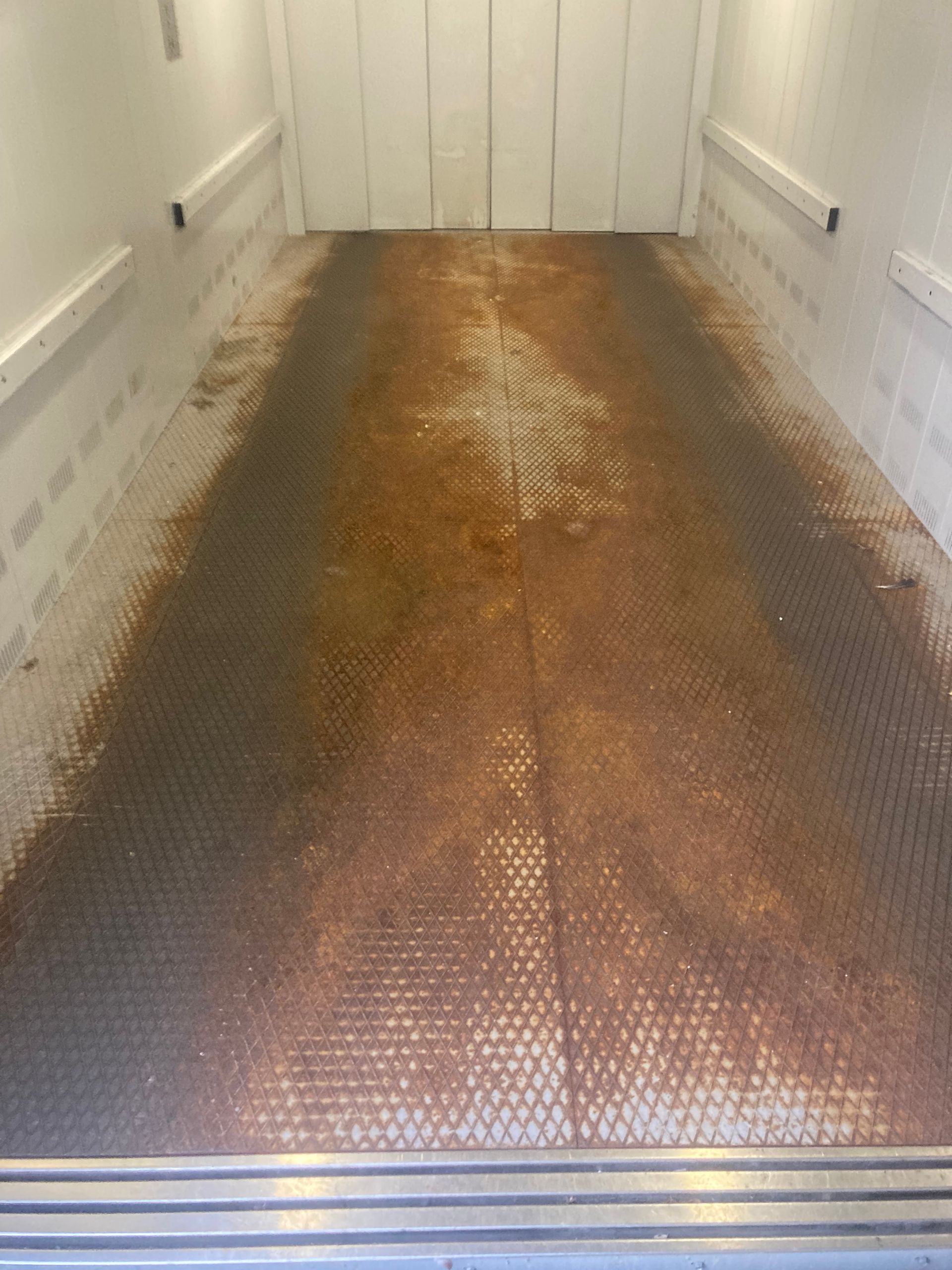 Ein rostiger Metallboden in einer Garage mit einer weißen Wand.