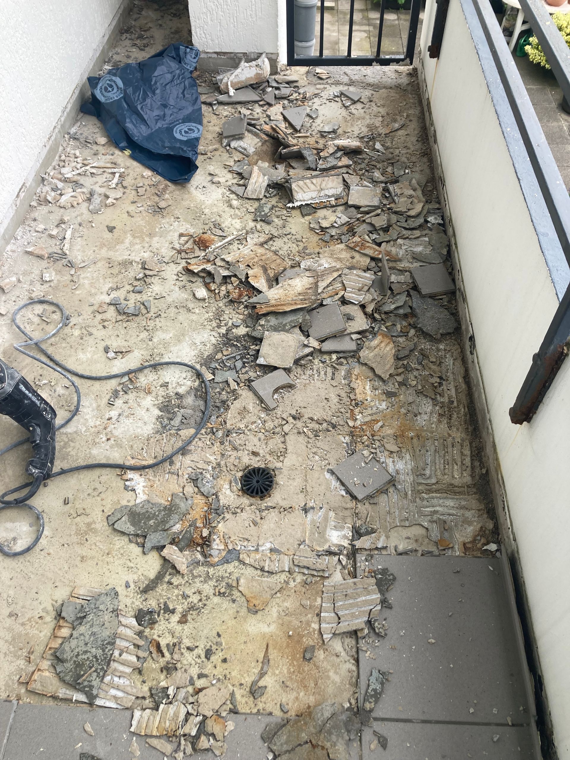 Balkon mit Fliesenentfernung im Gange; Schutt, Werkzeuge und eine dunkle Plane sind vorhanden.