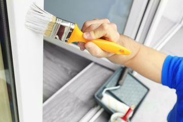 Maler streicht einen Fensterrahmen in Weiß