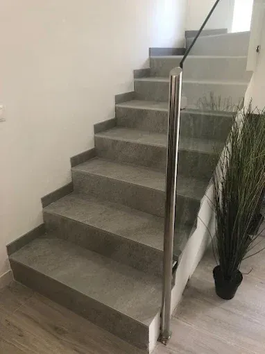 Escalera de baldosas grises con barandilla cromada y planta en maceta.