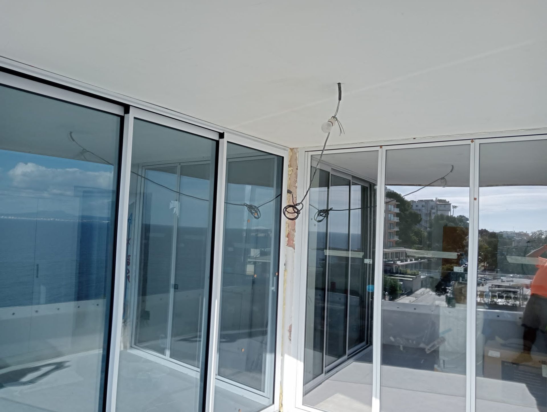 Un balcón con puertas corredizas de vidrio. Cables cuelgan del techo. Un obrero de la construcción está de pie.