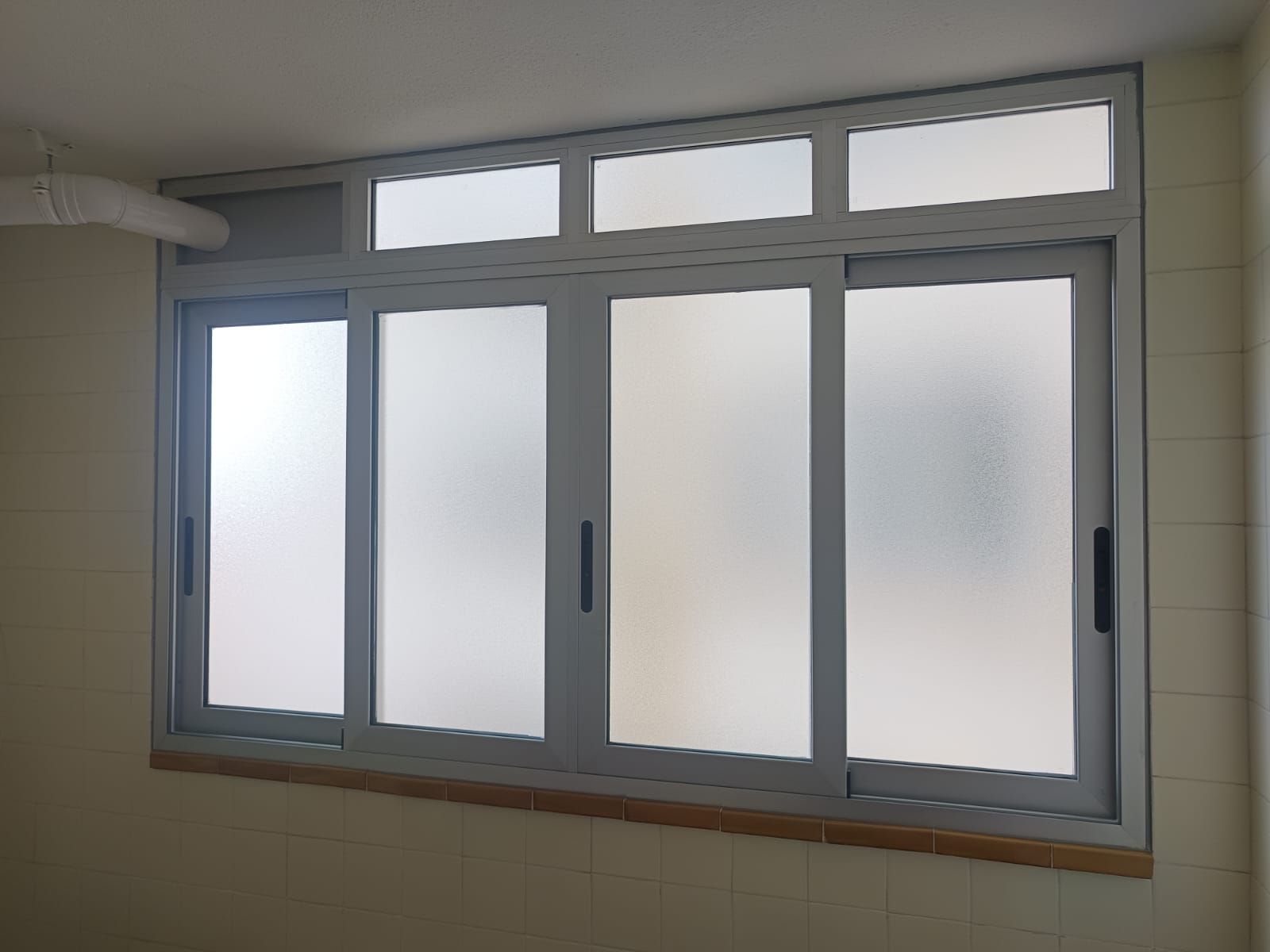 Ventana corrediza gris con paneles de vidrio esmerilado en una habitación.