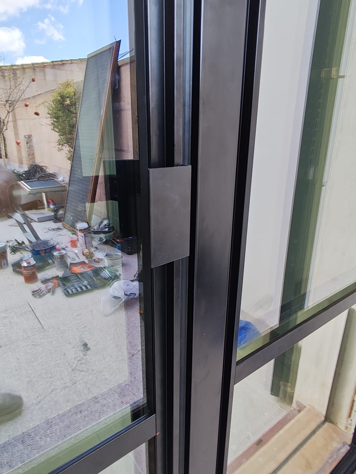 Ventana con marco negro y pestillo metálico oscuro. Afuera hay una obra en construcción.