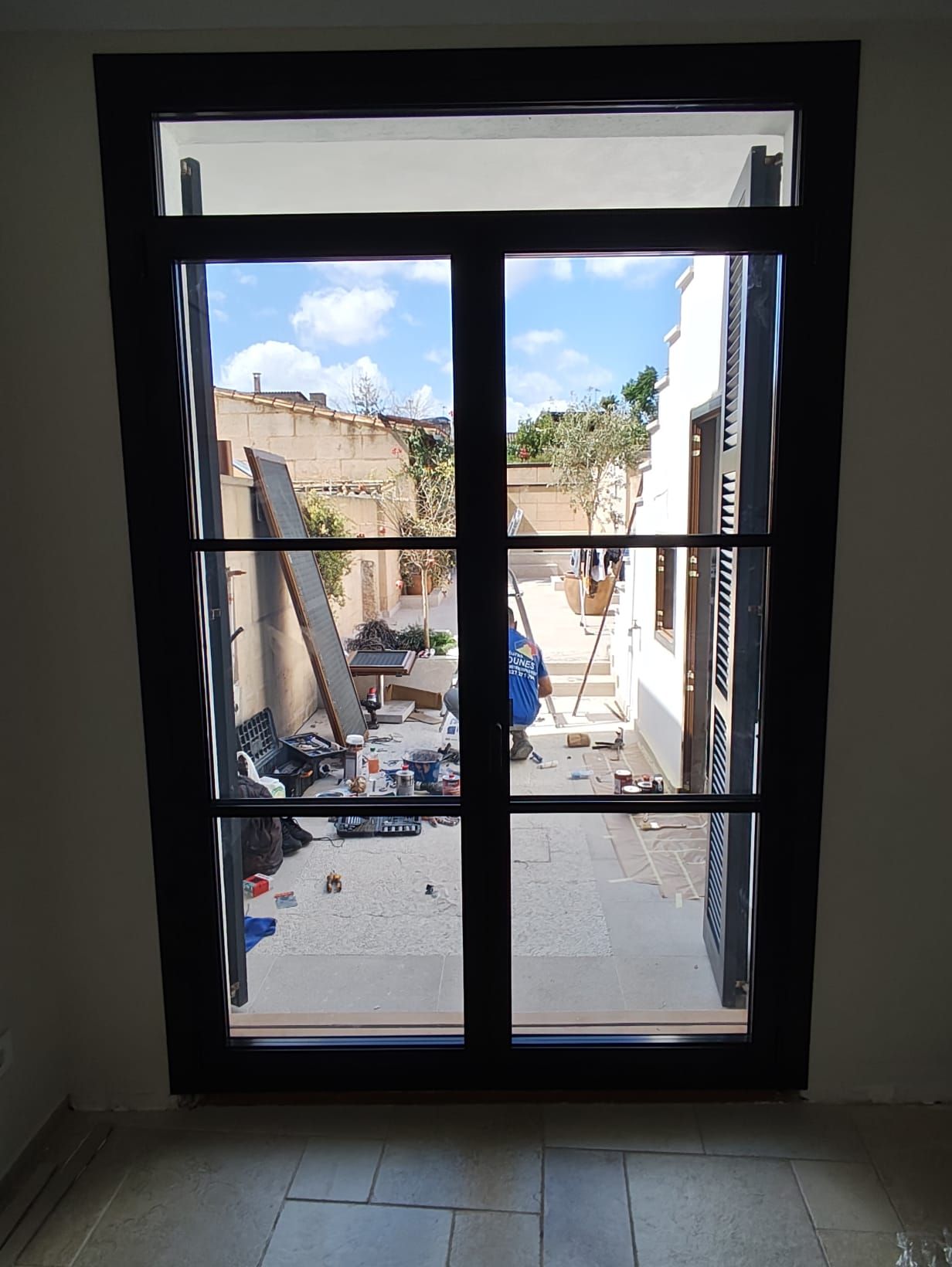 Ventana con marco negro que da a un patio con materiales de construcción, cielo azul.