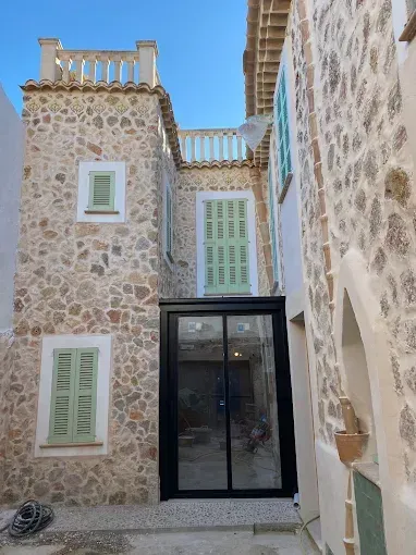 Un estrecho callejón de piedra con una moderna puerta de entrada de cristal negro.