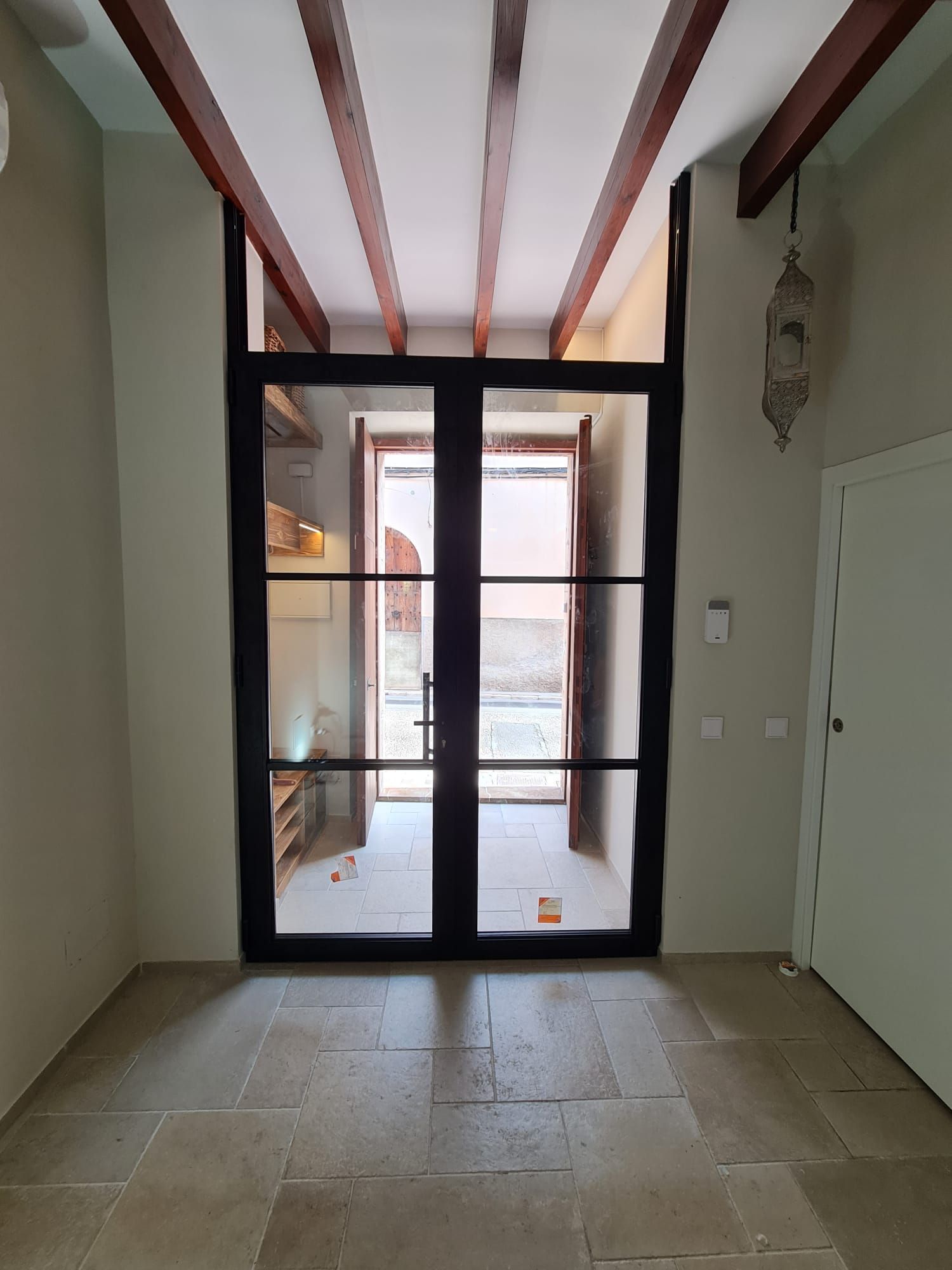 Las puertas de vidrio con marco negro conducen a un patio al aire libre con pisos de piedra beige