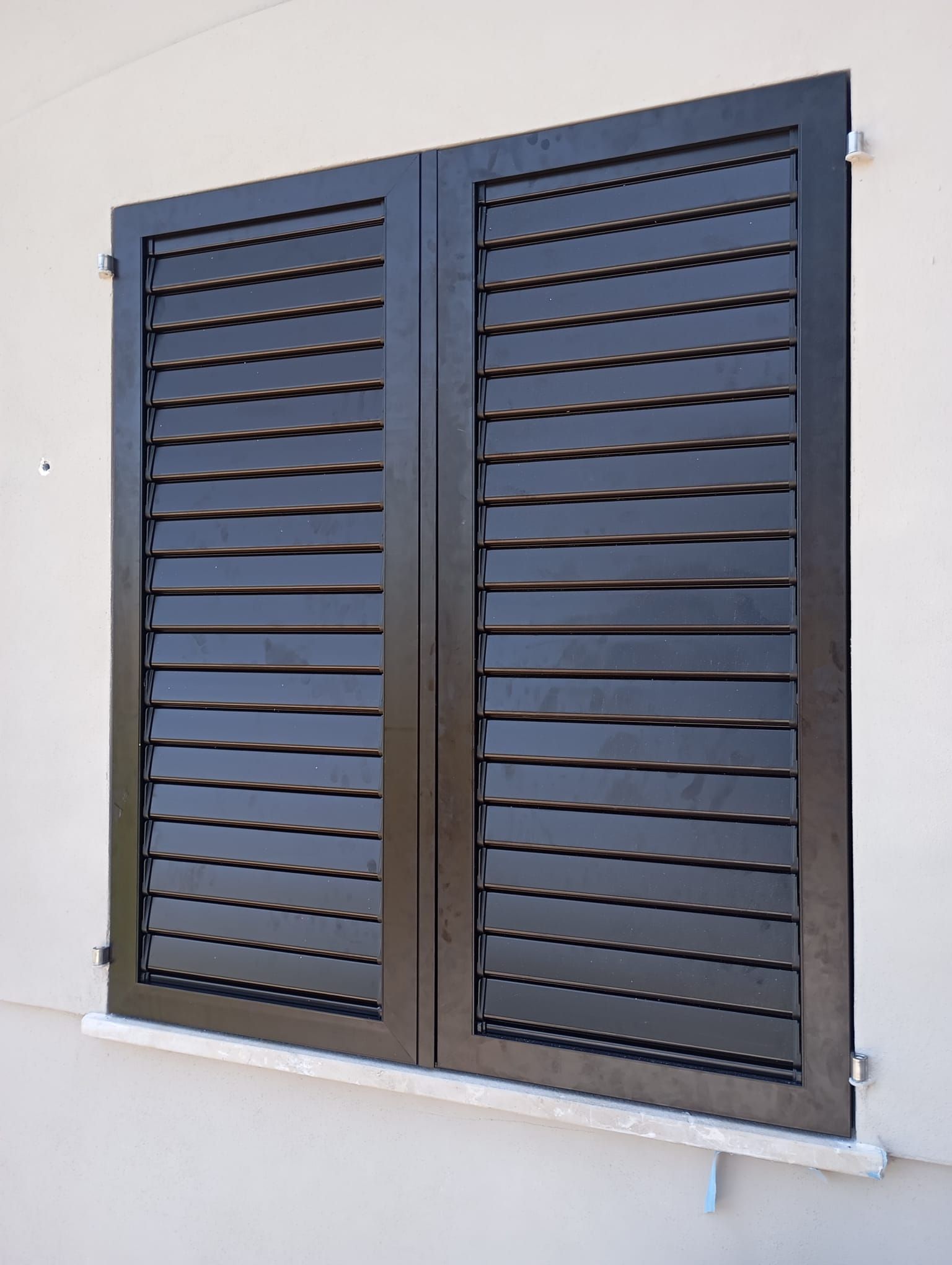Persianas negras con lamas en un edificio blanco, cerradas.