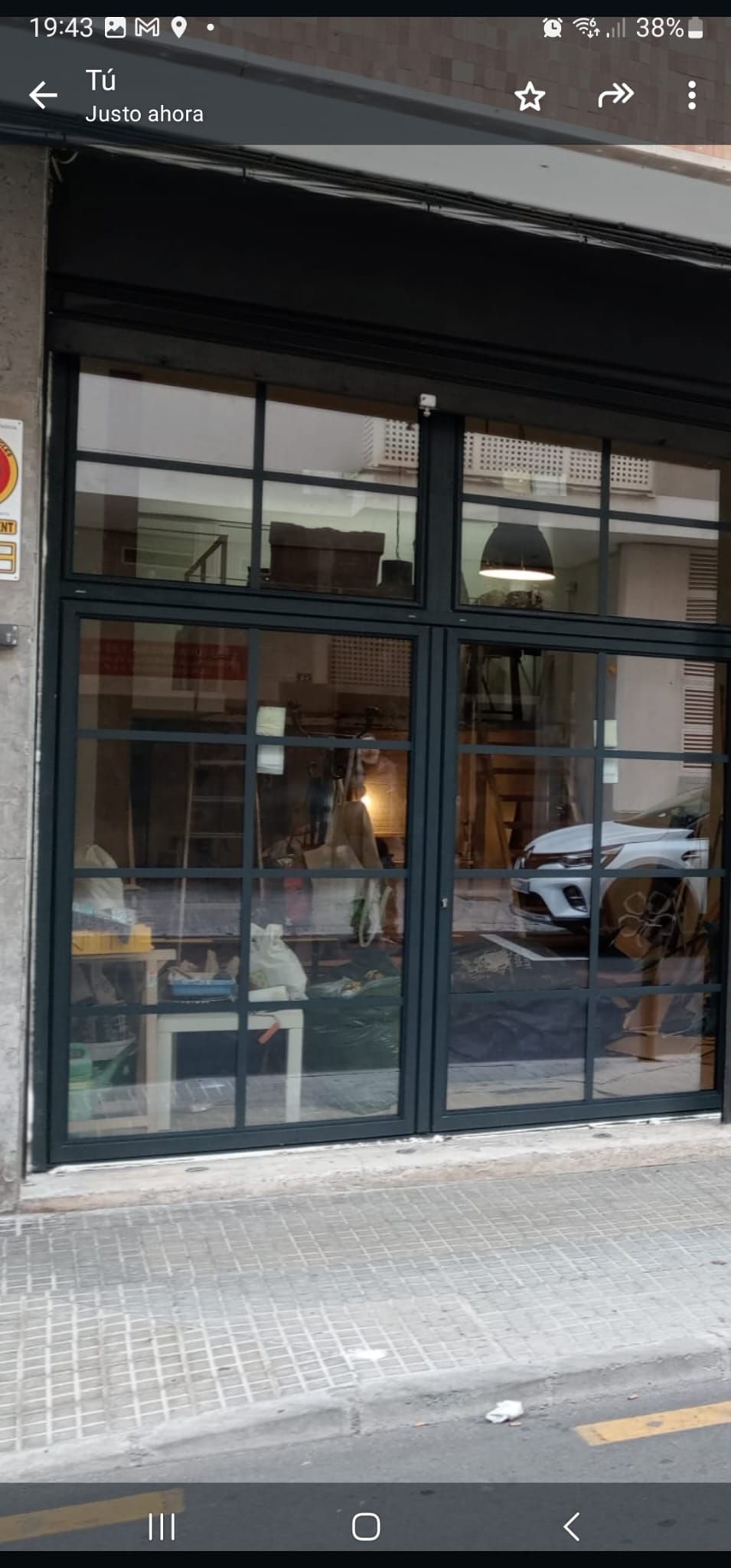 Una tienda con escaparates y marco negro. En el interior se ven varios artículos y el reflejo de un coche.