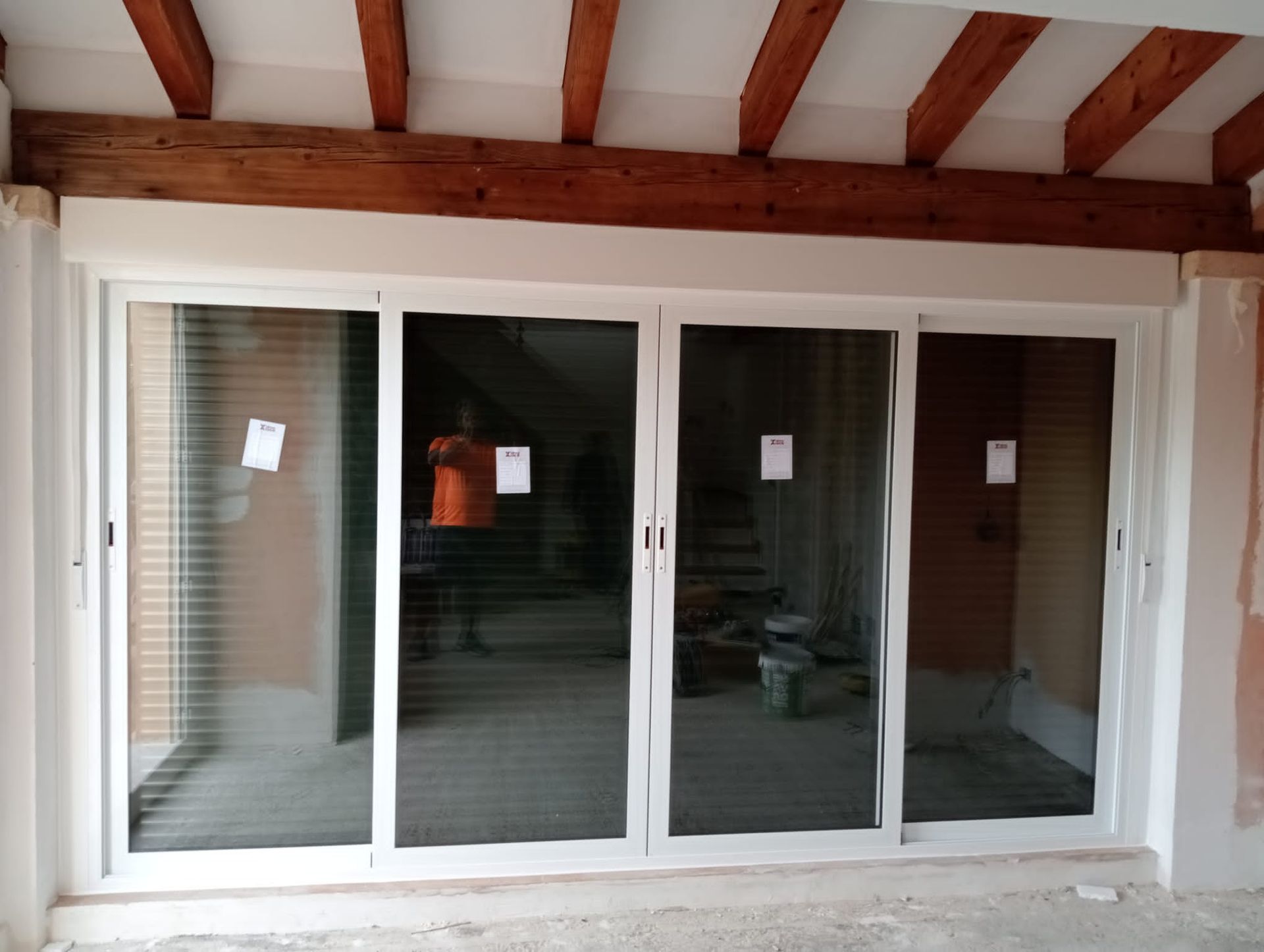 Puertas corredizas de vidrio con marcos blancos y cuatro paneles, bajo vigas de madera a la vista.