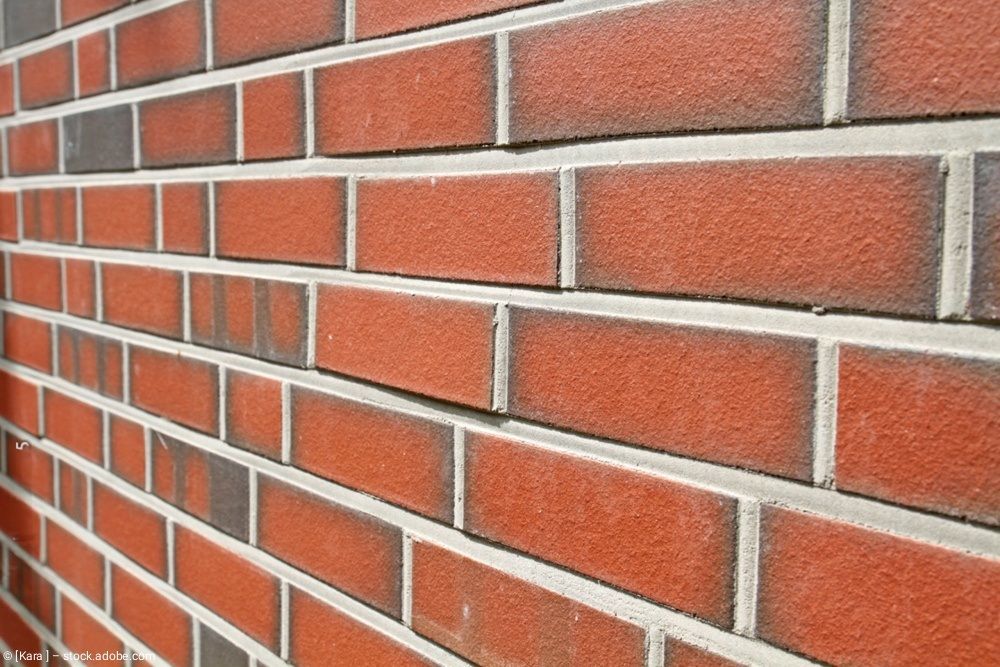Nahaufnahme einer roten Backsteinmauer mit weißen Fugen, aus einem bestimmten Winkel betrachtet.