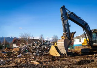 Baustelle mit einem Kran neben einem Gebäude, das unter blauem Himmel mit Gerüsten und weißen Schutzplanen verhüllt ist