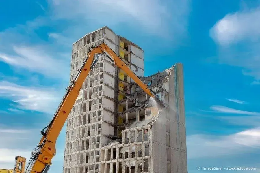 Ein Baukran demontiert vor blauem Himmel ein hohes Betongebäude
