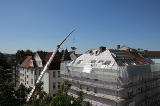 Bauarbeiten auf einem Stadtdach mit einem Kran neben einem im Umbau befindlichen Gebäude an einem klaren Tag