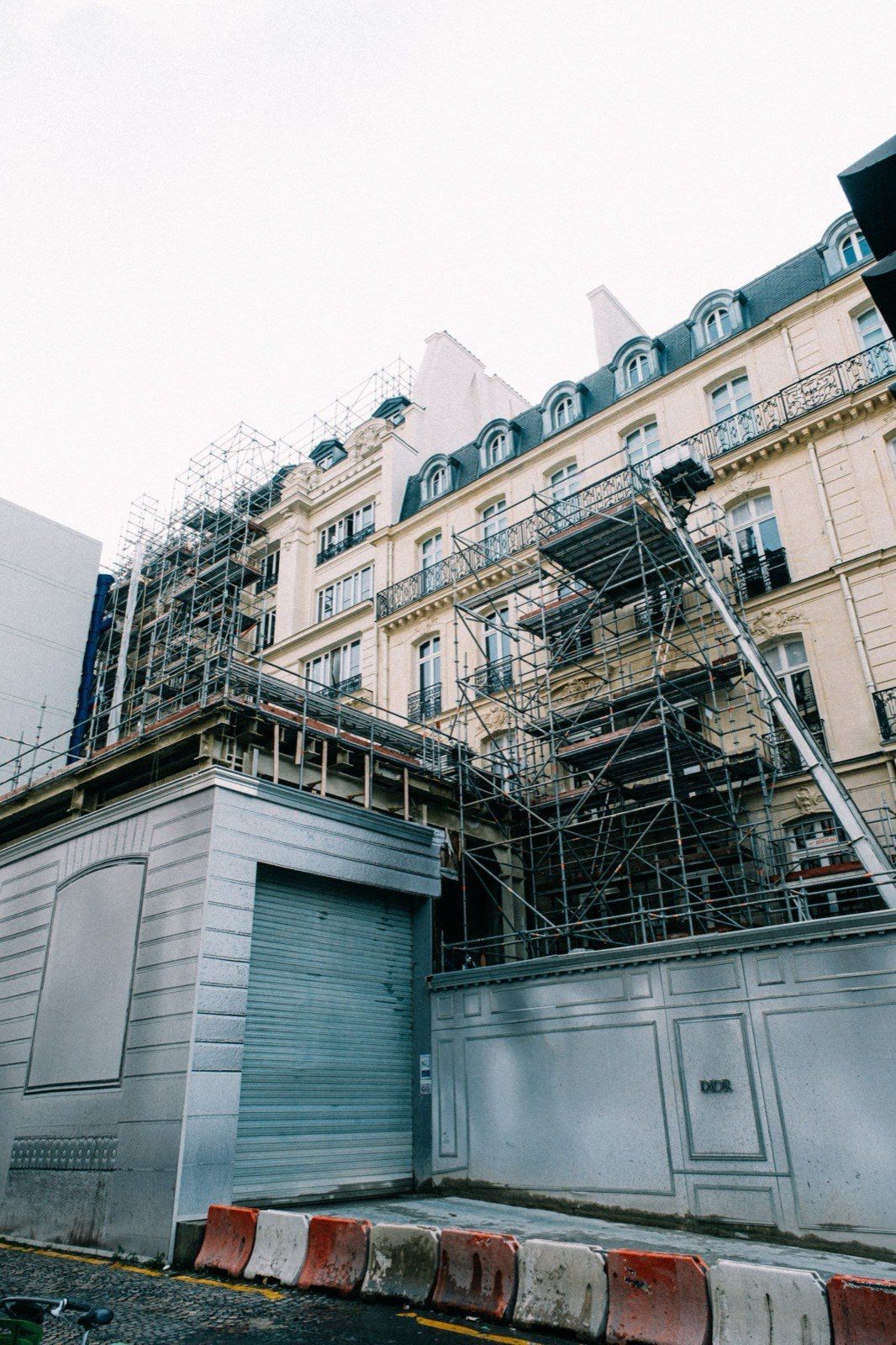 Baustelle mit einem Kran neben einem Gebäude, das unter blauem Himmel in ein Gerüst und weiße Schutzplanen gehüllt ist