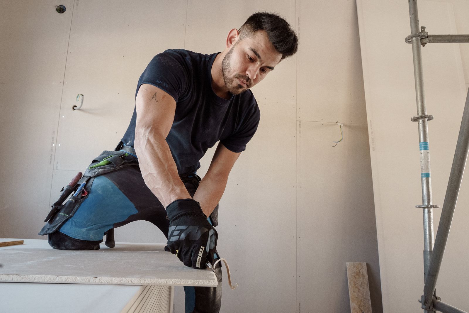 Mann kniet auf einer Werkbank und misst oder schneidet Material während einer Hausrenovierung.