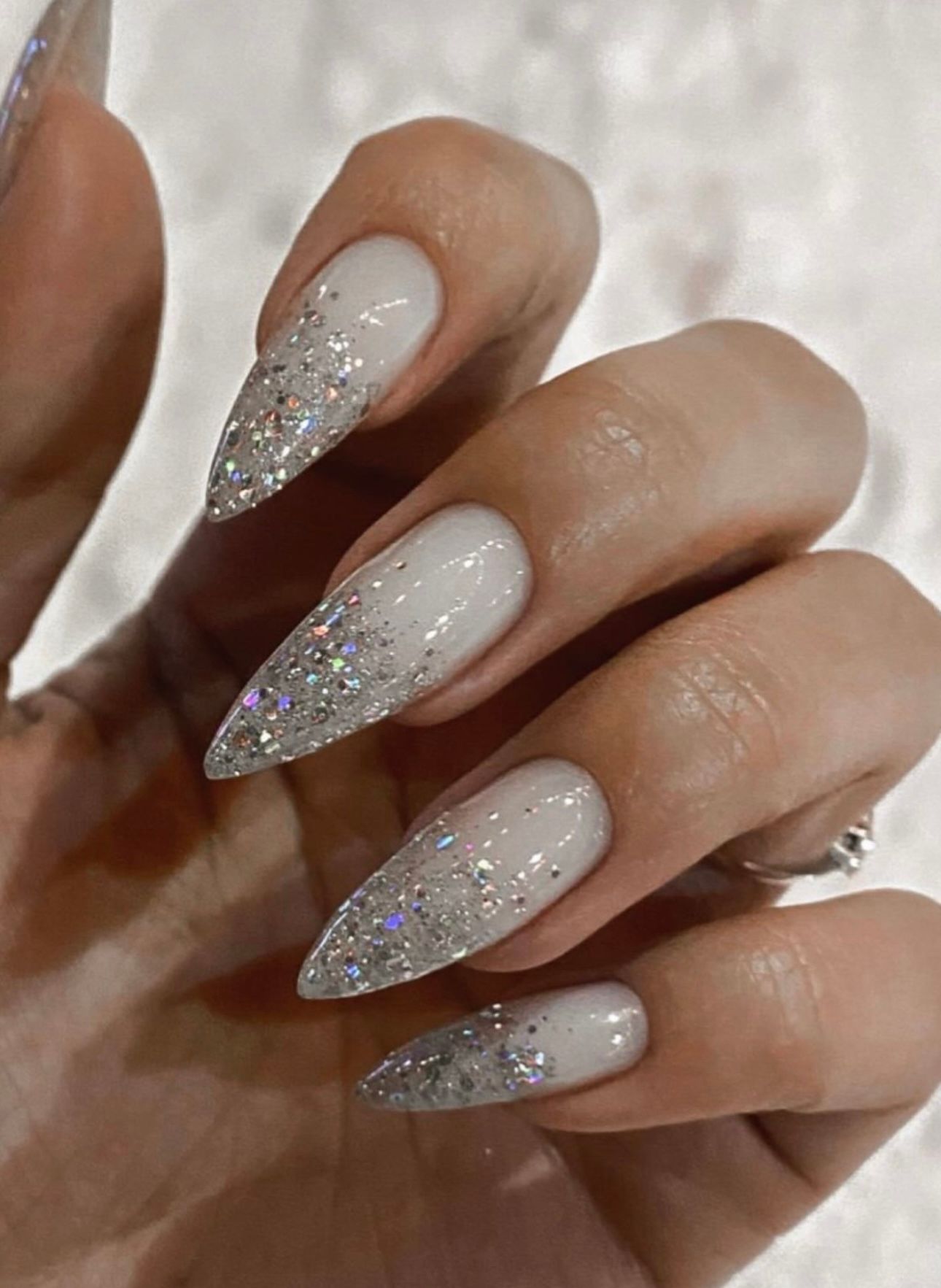 Eine Nahaufnahme der Nägel einer Person mit weißem und silbernem Glitzer.