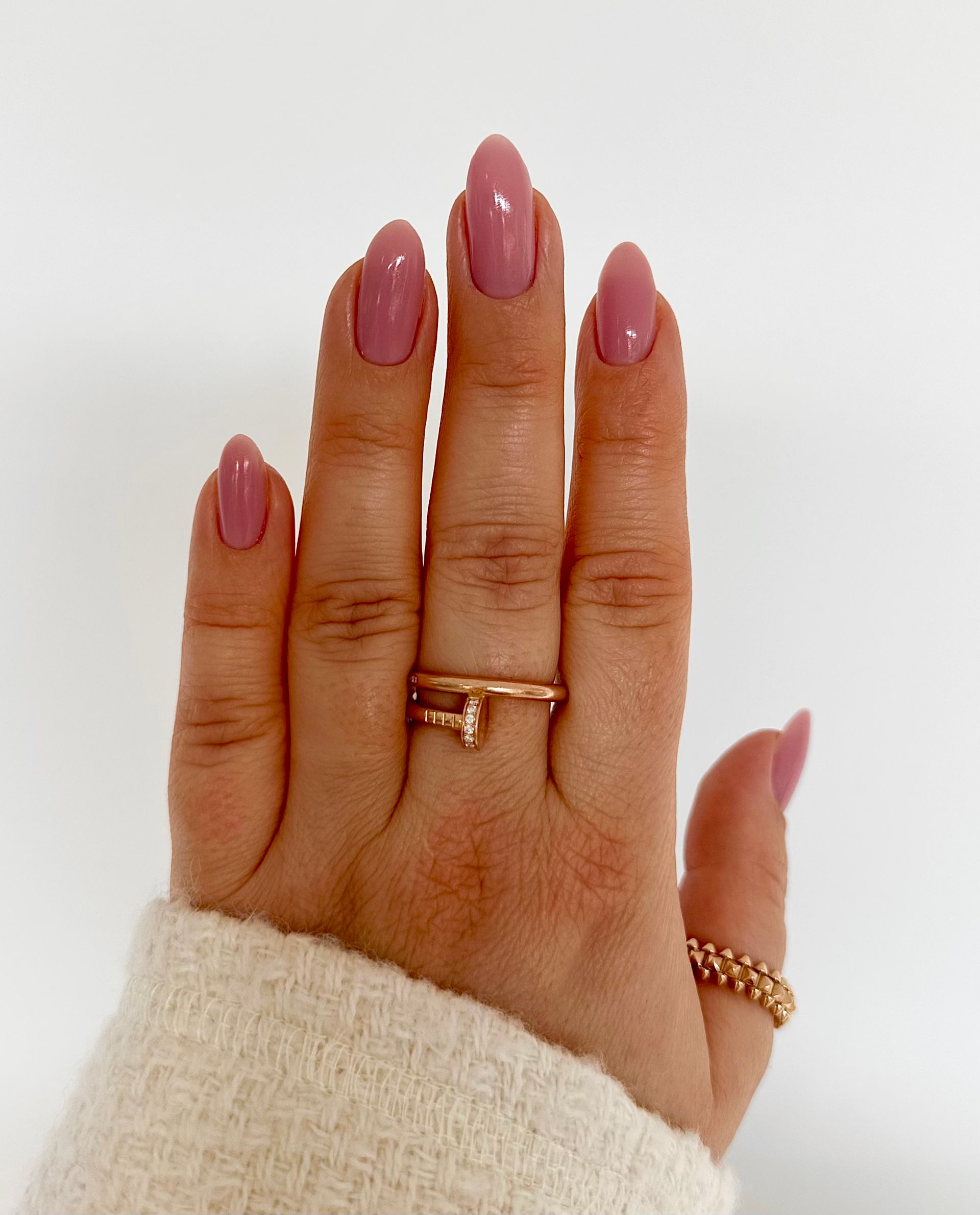 Eine Frauenhand mit rosa Nägeln und einem goldenen Ring