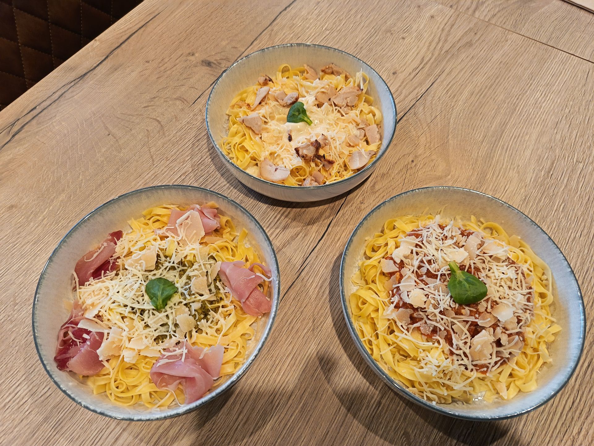Trois bols de pâtes avec différentes garnitures sur une table en bois.