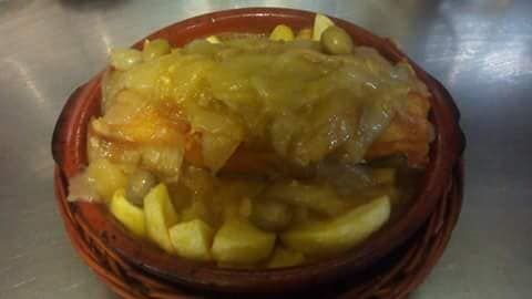 Uma tigela de comida com batatas e cebolas sobre uma mesa.