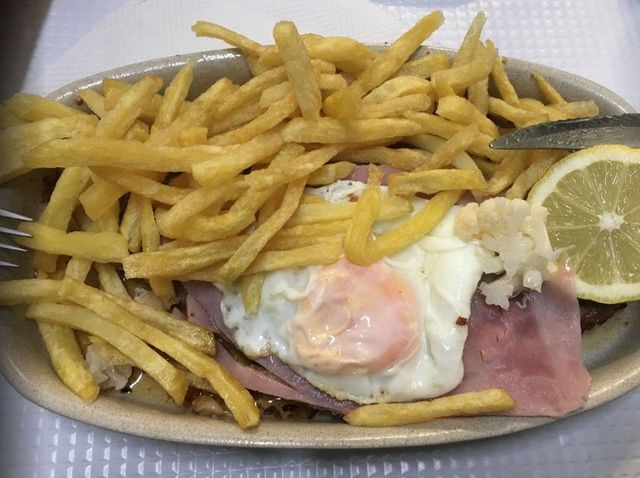 Um prato de comida com batatas fritas, presunto, ovos e uma rodela de limão.
