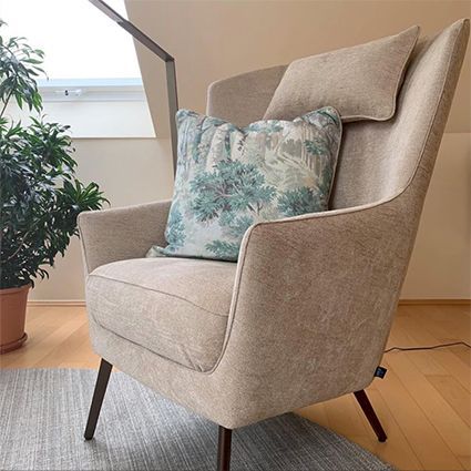 Hellbrauner Sessel mit blau gemustertem Kissen; links eine Topfpflanze.