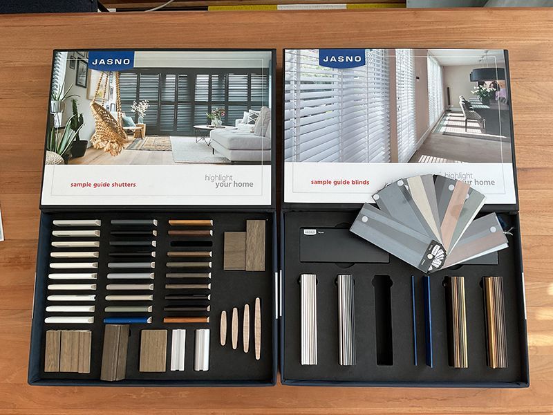 Zwei offene Mustersets auf einem Tisch zeigen Fenster- und Türoptionen, einschließlich Farbmustern und Materialien.