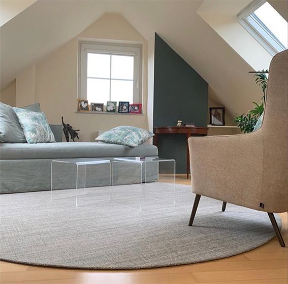 Gemütliches Wohnzimmer mit grauem Sofa, beigem Sessel und rundem Teppich. Dachboden mit abgewinkelten Wänden und Fenster.