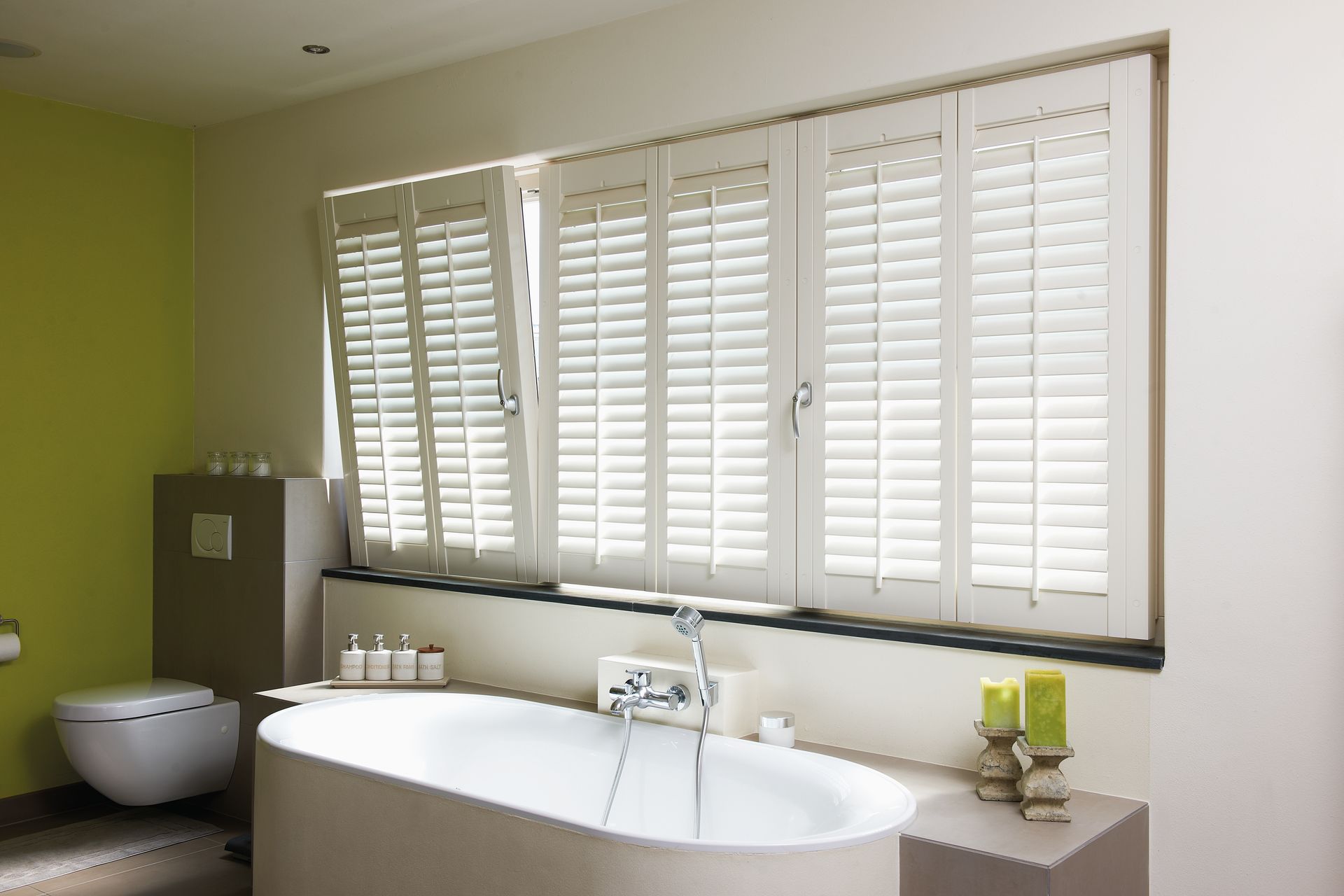 Badezimmer mit weißer Badewanne, weißen Fensterläden und grüner Akzentwand.