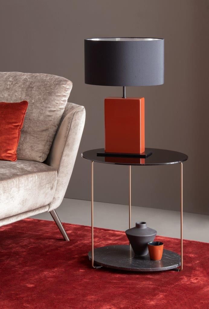 Moderne Wohnzimmerszene mit Lampe auf schwarzem Beistelltisch, rotem Teppich und Kissen.