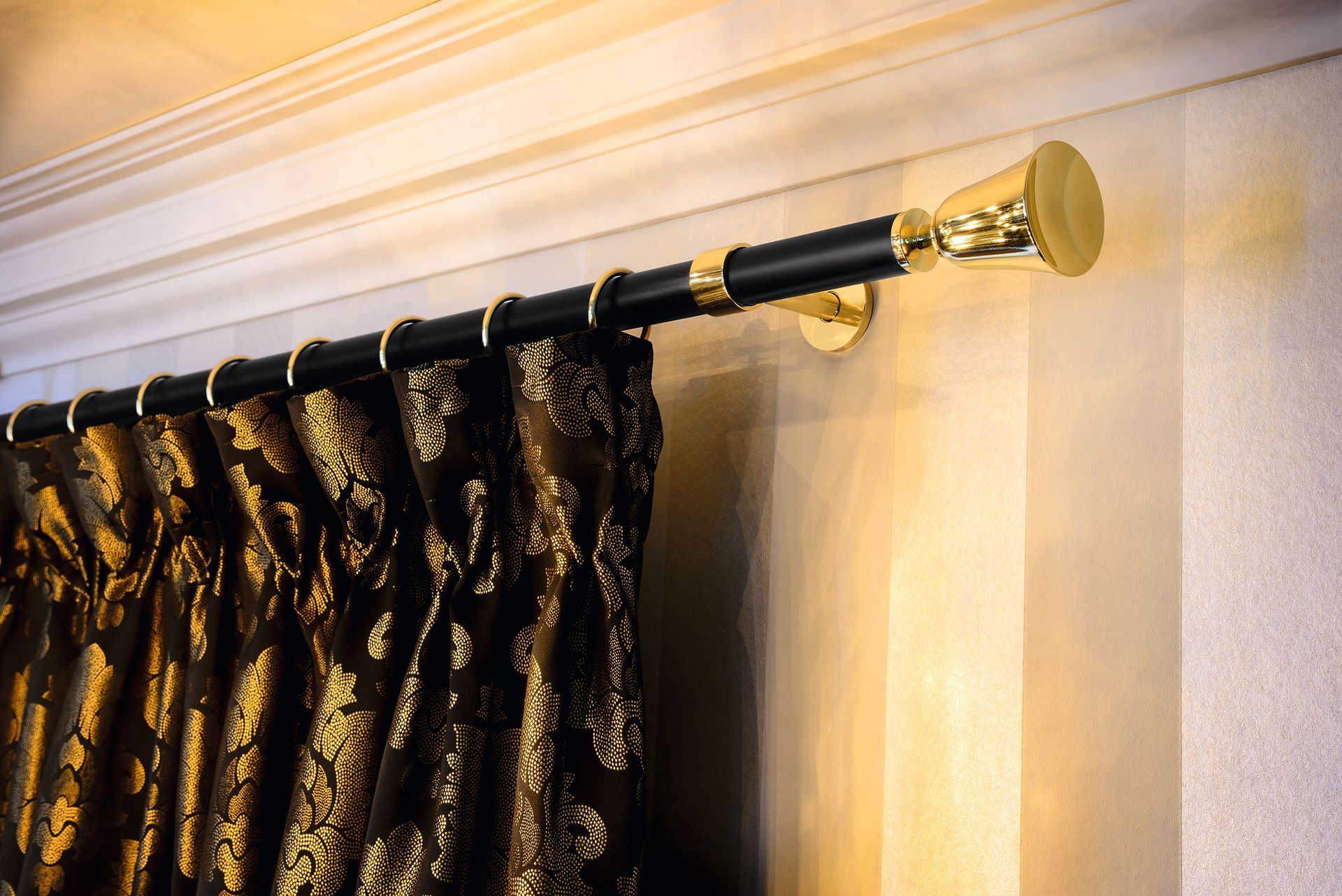 Schwarz-goldene Gardinenstange mit einem gemusterten braunen Vorhang vor einer beigen Wand.