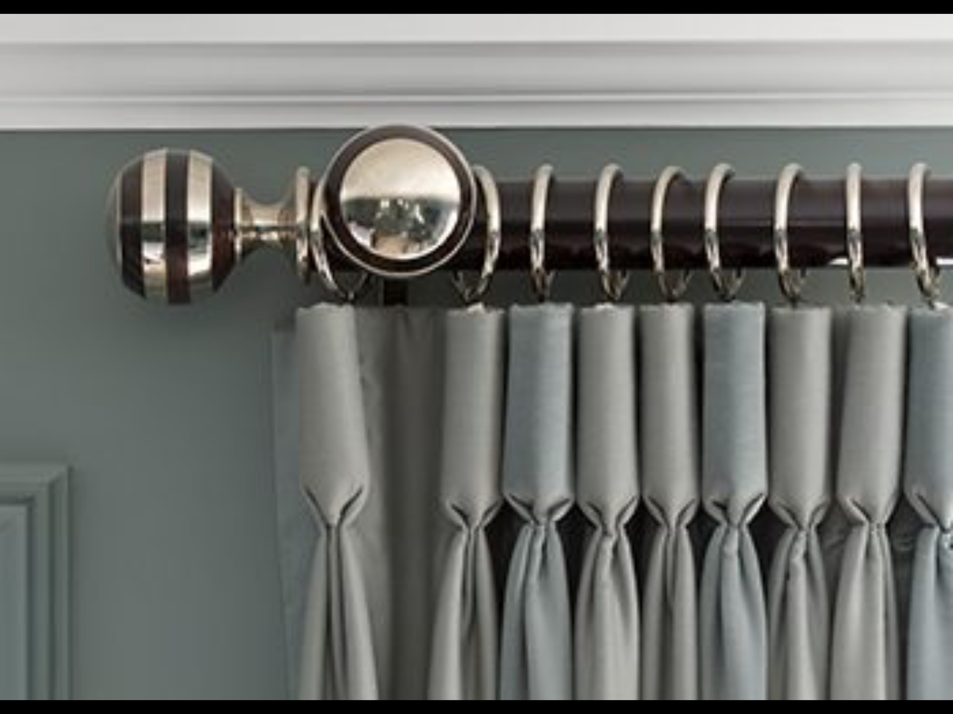 Nahaufnahme von Vorhängen mit dekorativer Stange, silbernen Ringen und gestreiftem Endstück. Vorhänge sind blau/grau.
