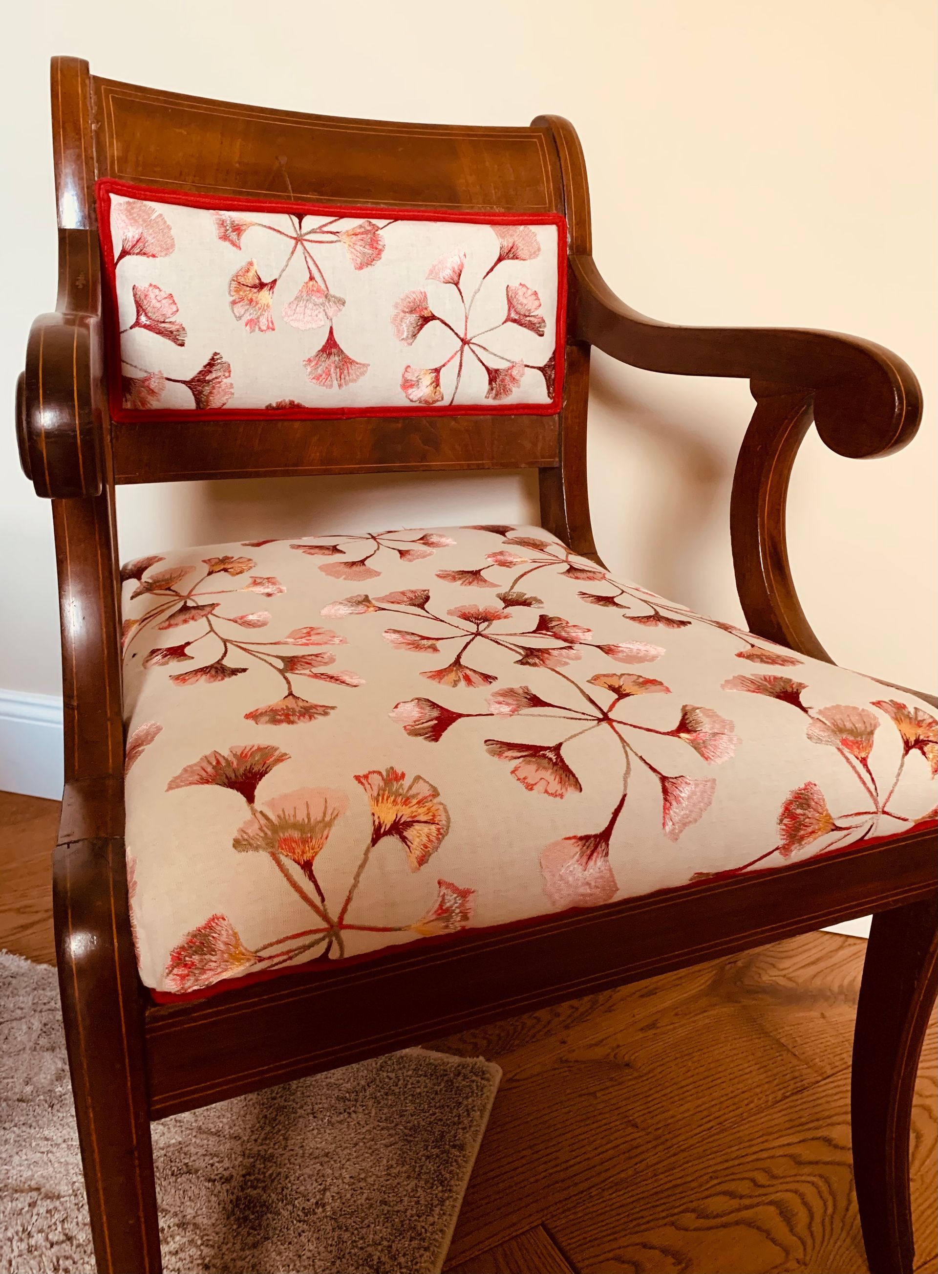 Holzsessel mit beiger Polsterung mit Blumenmuster und roten Verzierungen.