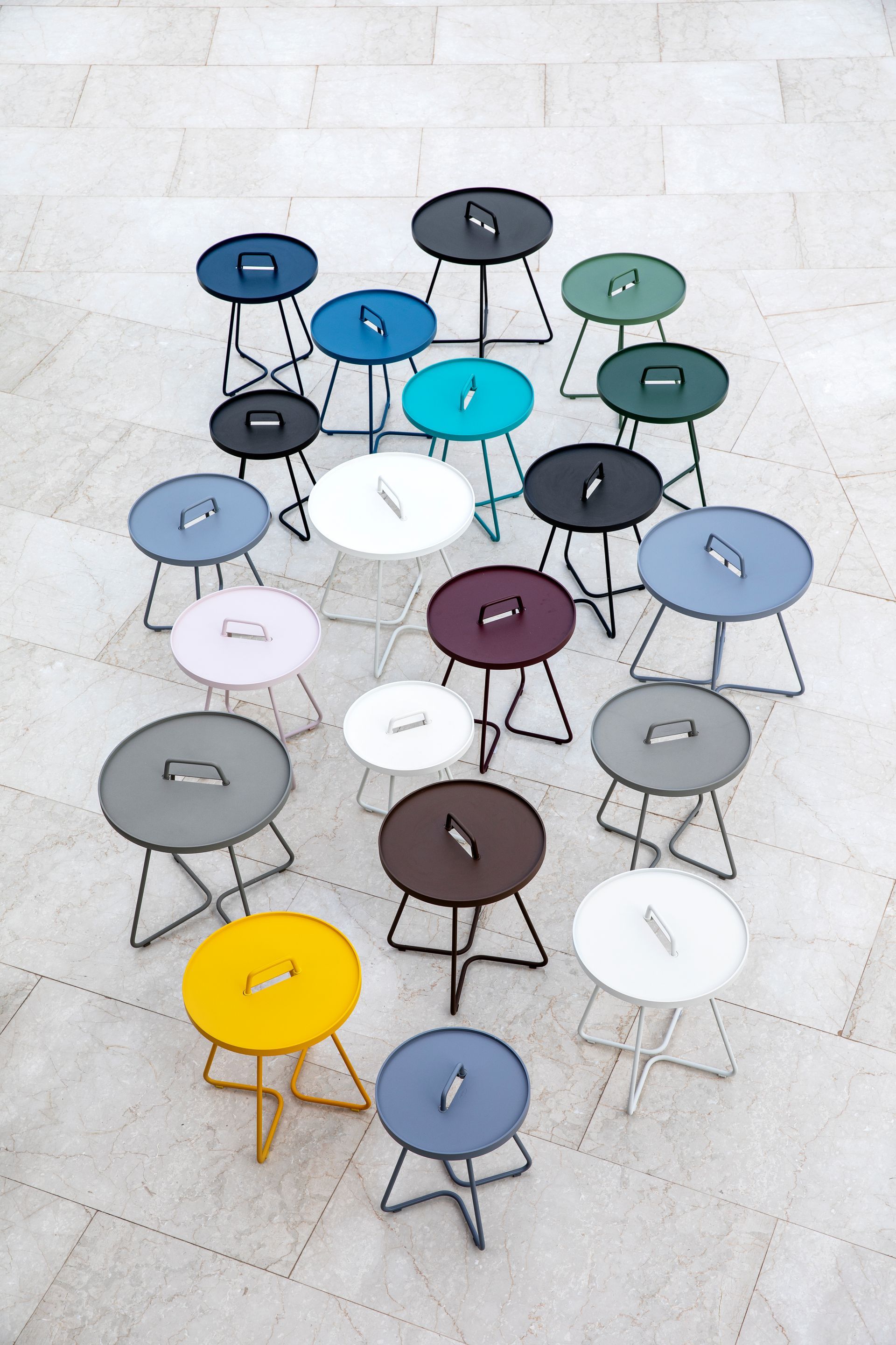 Eine Sammlung farbenfroher, runder Hocker mit Metallrahmen, angeordnet auf einem strukturierten Boden.