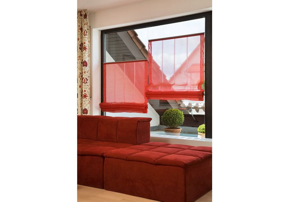Rote Raffrollos an einem Fenster mit Blick auf einen Hinterhof. Rotes Sofa davor.