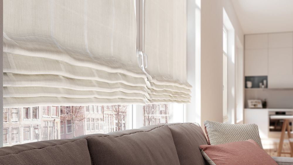 Beige Raffrollos bedecken teilweise das Fenster, in der Nähe eines braunen Sofas und einer Küche.