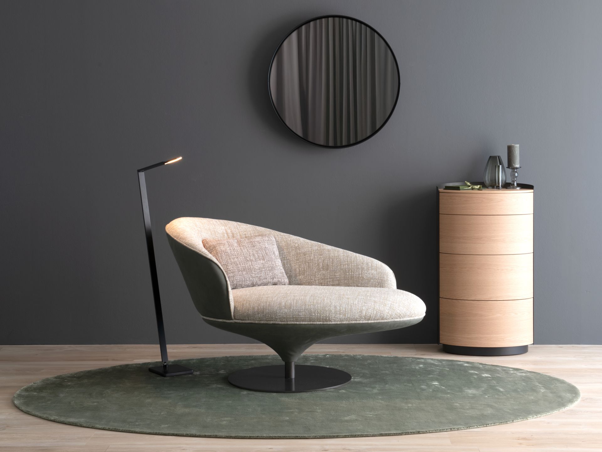 Modernes Wohnzimmer: hellgrauer Stuhl, runder grüner Teppich, schwarze Lampe, Holzschrank, runder Spiegel, graue Wand.