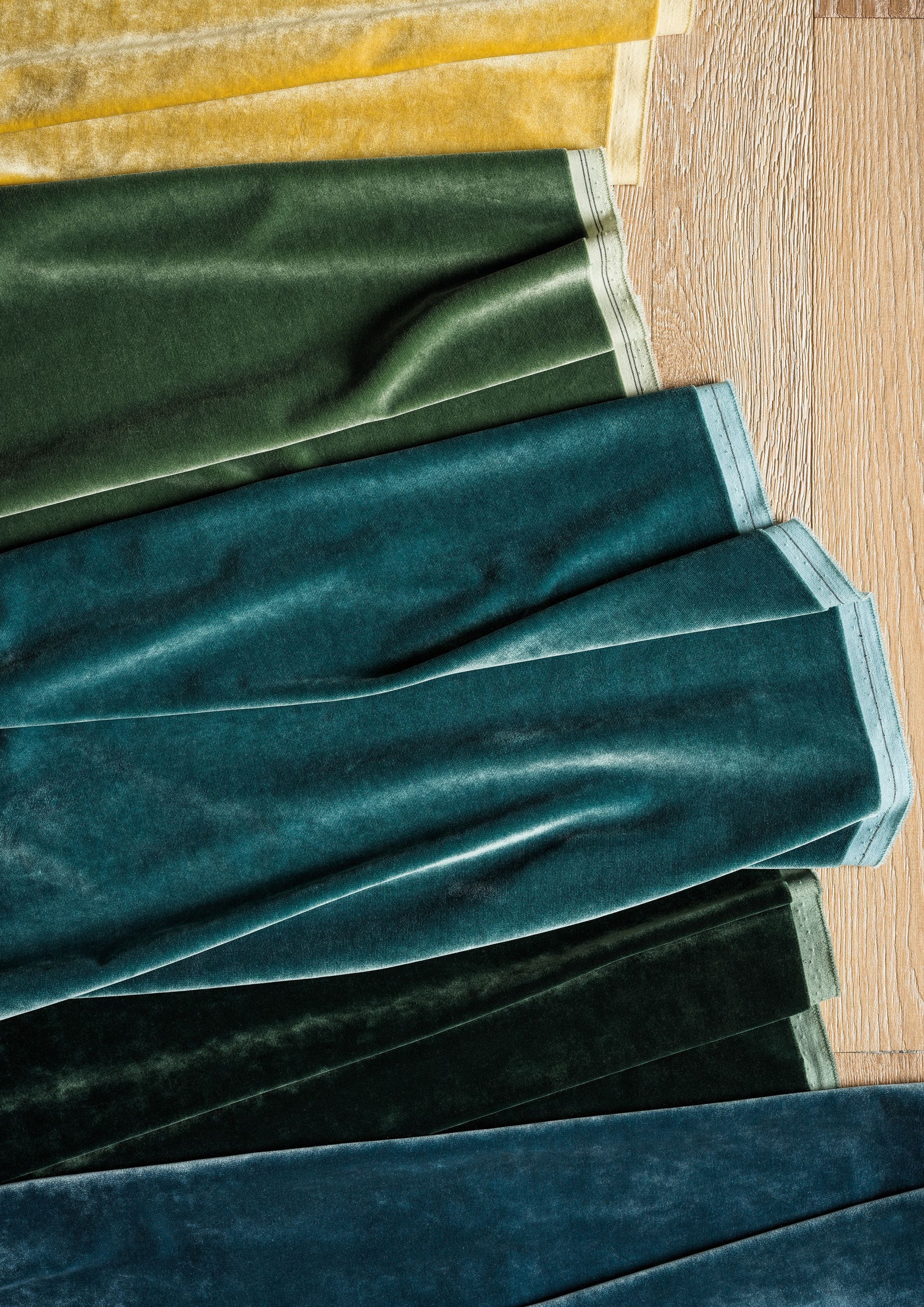 Nahaufnahme von gestapelten Samtstoffmustern in Gelb-, Grün- und Blautönen.