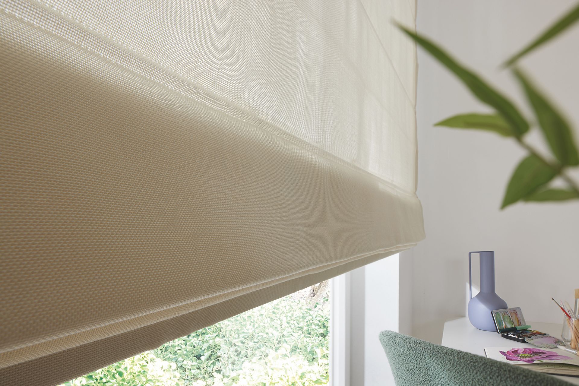 Beiges Raffrollo, teilweise heruntergelassen, neben einem Fenster.
