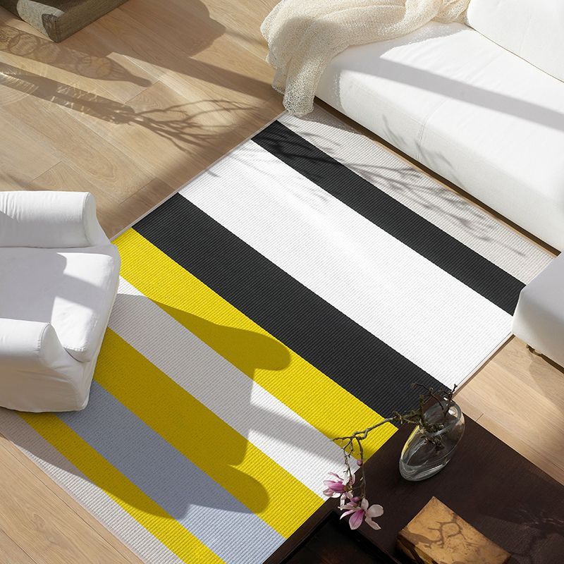 Ein gestreifter Teppich mit schwarzen, gelben und weißen Streifen in einem Wohnzimmer mit weißen Möbeln.