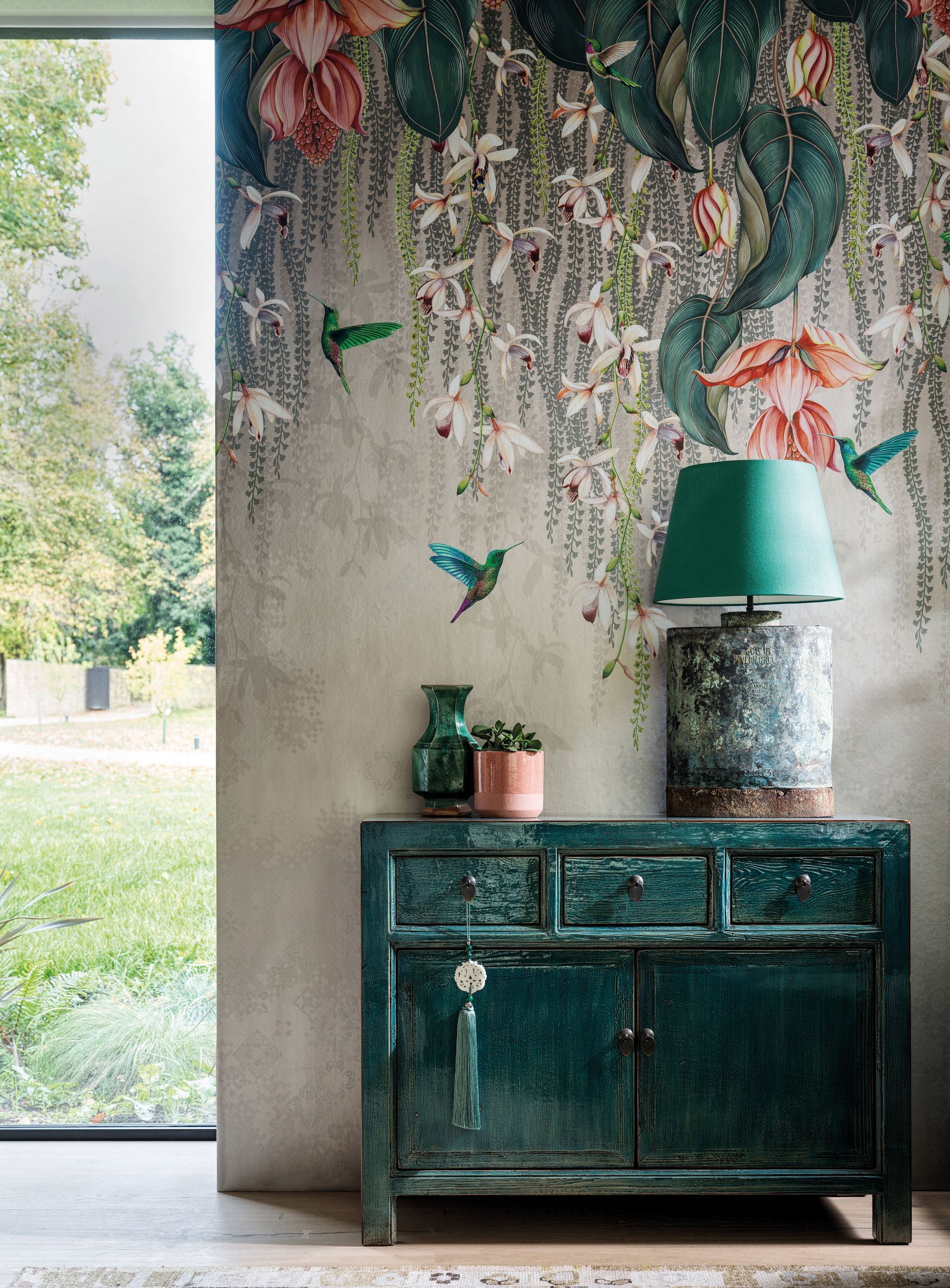 Grüner Schrank mit Lampe und Kolibri-Tapete neben dem Fenster mit Blick auf einen grünen Rasen.