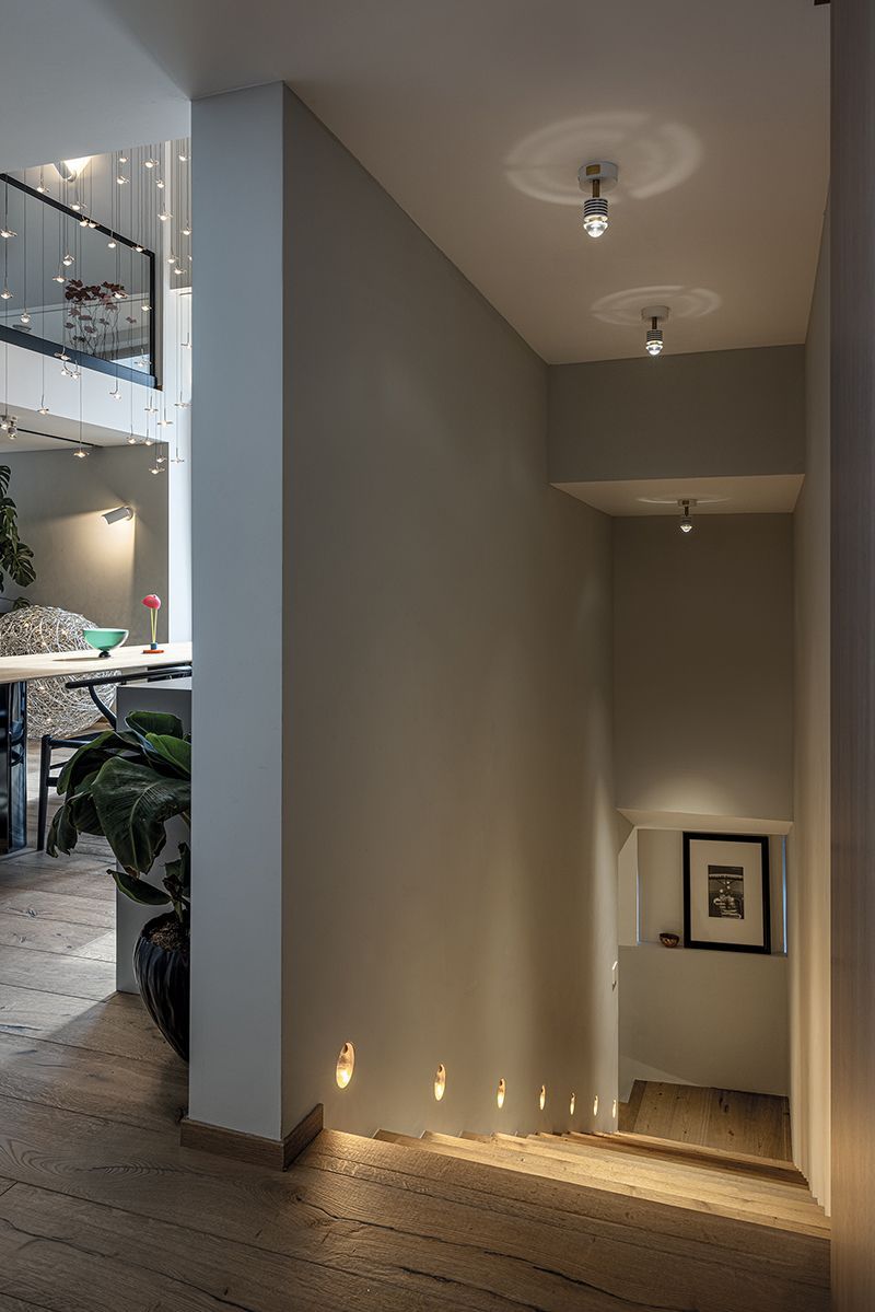 Flur mit absteigender Treppe, beleuchtet durch Einbauleuchten im Boden und in der Decke.