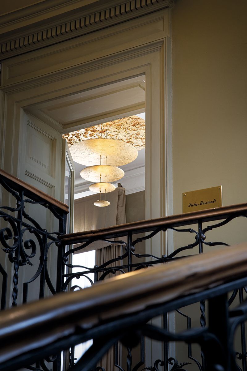 Eine Treppe führt zu einem Raum mit hängenden Stufenlampen. Verziertes Geländer; lichtdurchfluteter Raum.