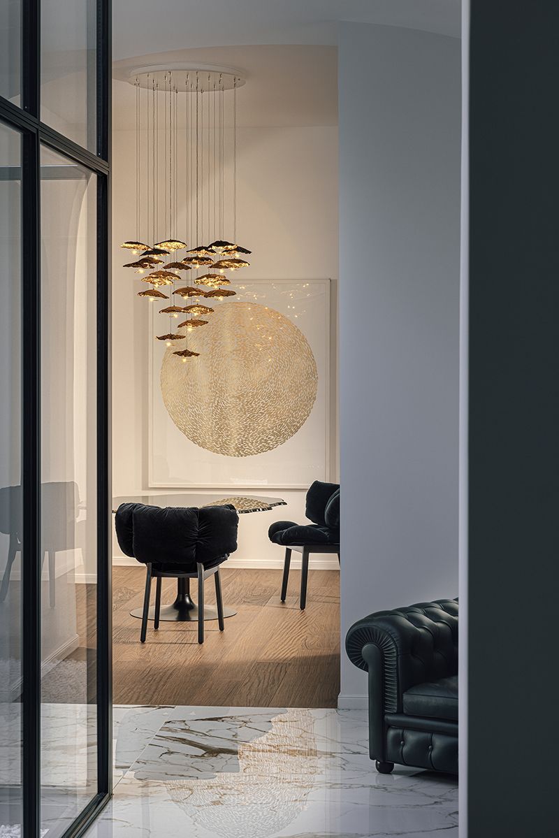 Inneneinrichtung mit Essbereich, schwarzen Stühlen, goldenem Kronleuchter und großen Kunstwerken.