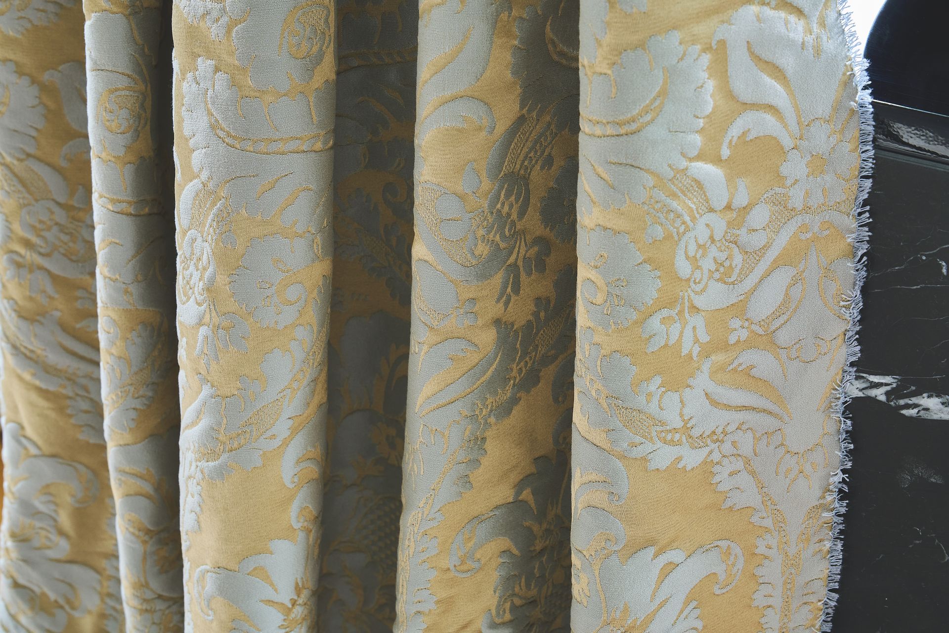 Stoff mit gold- und silberfarbenem Blumenmuster und vertikalen Falten.