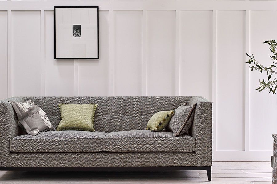 Graues Sofa mit gemusterten Kissen vor weißer Wandverkleidung, darüber Kunstwerk.