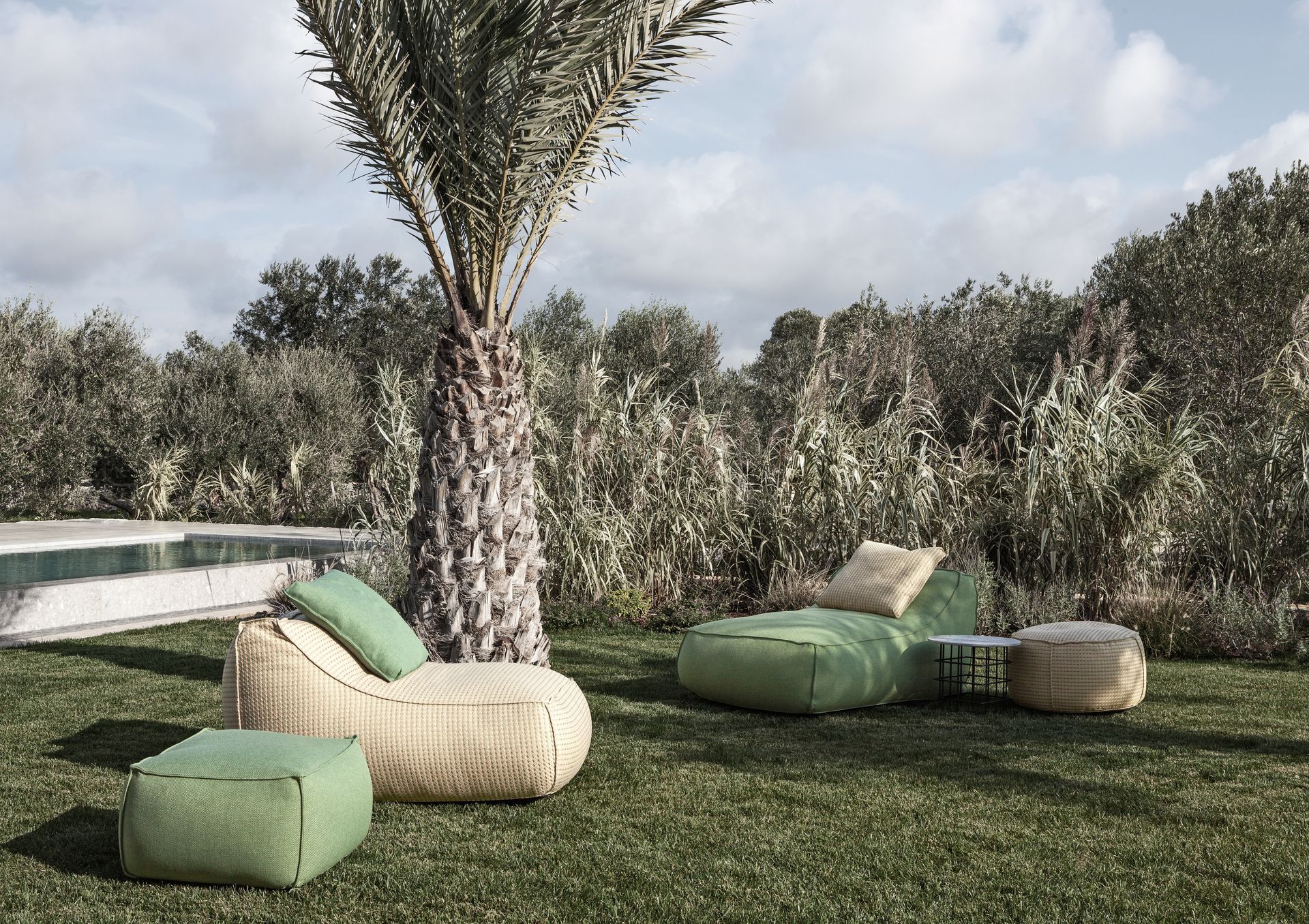 Grüner und beiger Sitzbereich im Freien neben einer Palme und einem Pool in einem grasbewachsenen Hof.